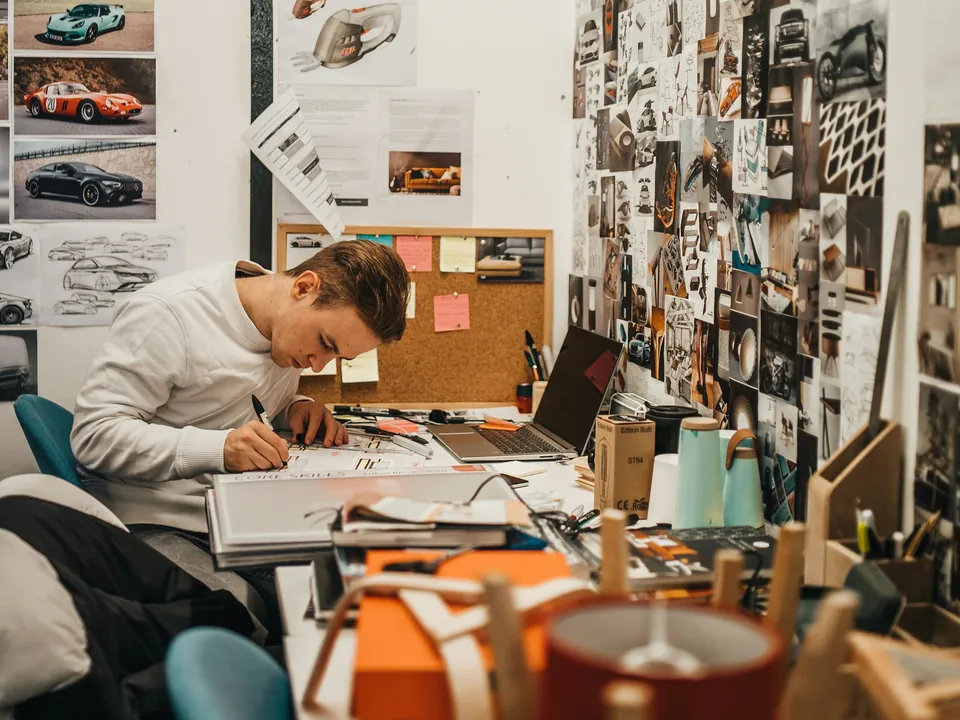 A designer sketching at his desk in a brand studio, the wall behind covered in reference images