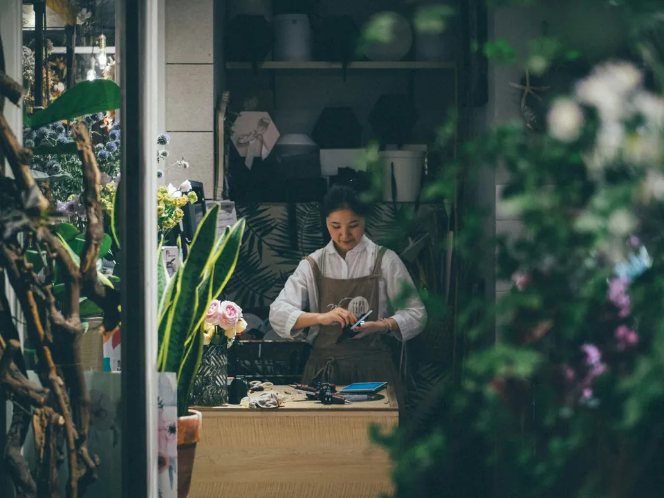 A florist at work at her bench, seen through flowers in the shop window