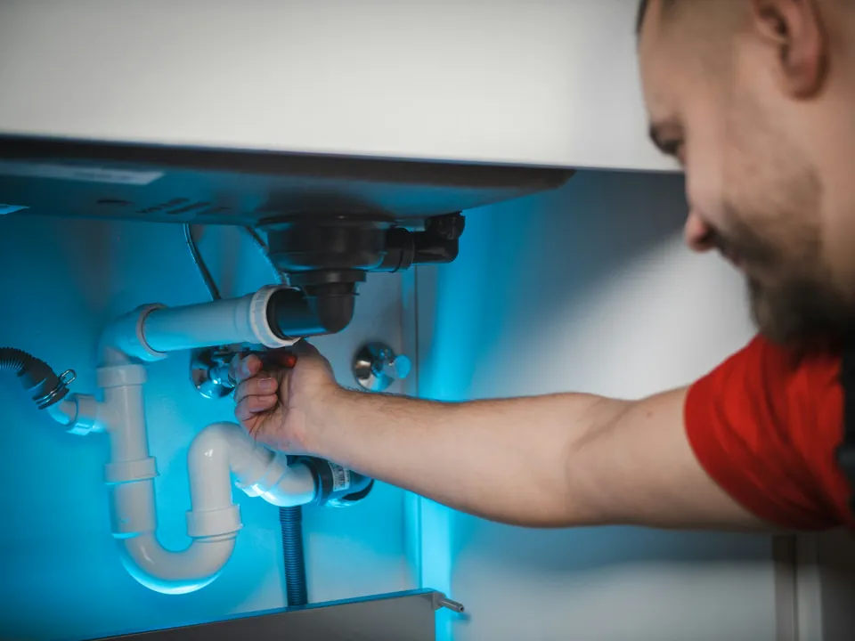 A plumber fitting a pipe under a sink