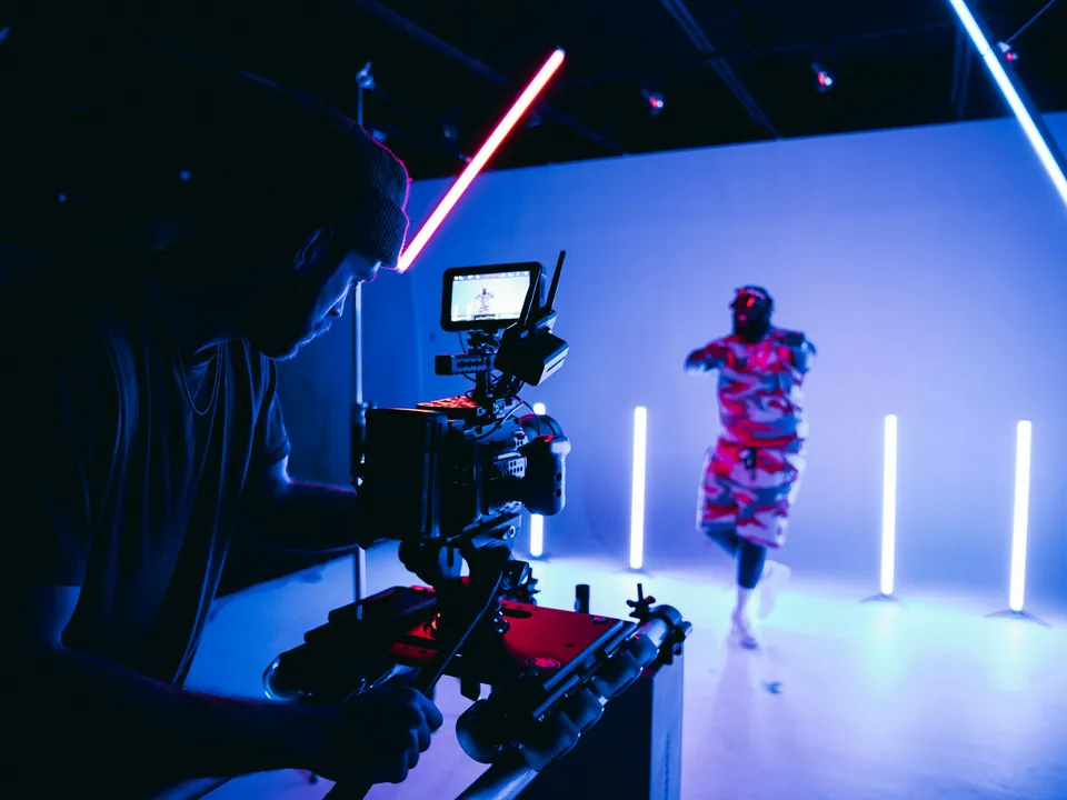 A camera operator filming a dancer on a neon-lit studio set